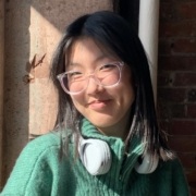 Headshot of Soomin Lee, wearing a green sweater, clear glasses, and blue headphones